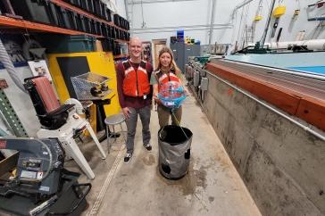 两名主要研究学生研究人员将他们赢得的海洋可再生能源设备放在波浪箱前. 他们穿着红色的救生衣.